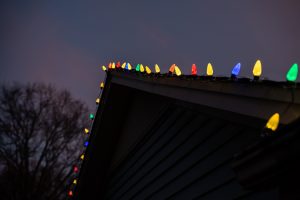 Roofline view of LED Christmas lights in red, yellow, blue, and green installed along a home’s gable edge.
