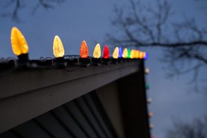 Close-up of multicolor C9 LED Christmas lights clipped along the gutter edge against a dark blue evening sky.