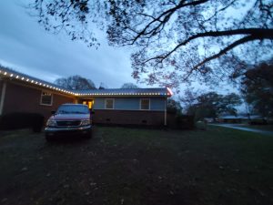 Single-story home with white holiday roofline lights installed at dusk, highlighting the gutter and roof edge.