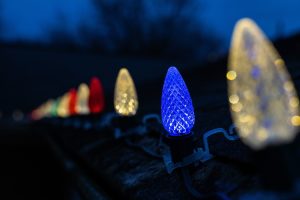 Macro shot of blue and warm white LED holiday bulbs clipped to a dark shingle roof during twilight.