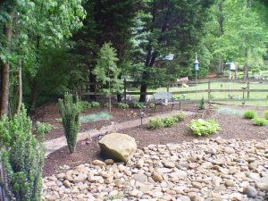Backyard hardscape features a dry creek bed with river rocks, brick path, bench seating, and layered planting.