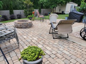Backyard patio with mixed paver stones, fire pit, lounge chairs, potted plants, and privacy fence.