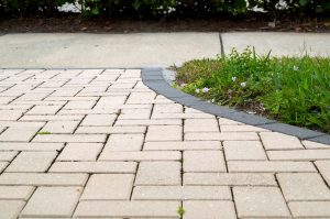 Curved herringbone paver walkway with black stone edge borders a mulched garden and meets a concrete sidewalk.