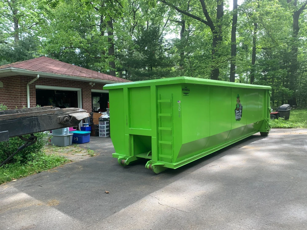Large green dumpster rental in a driveway near a garage to help you choose a size for remodel waste and cleanouts.
